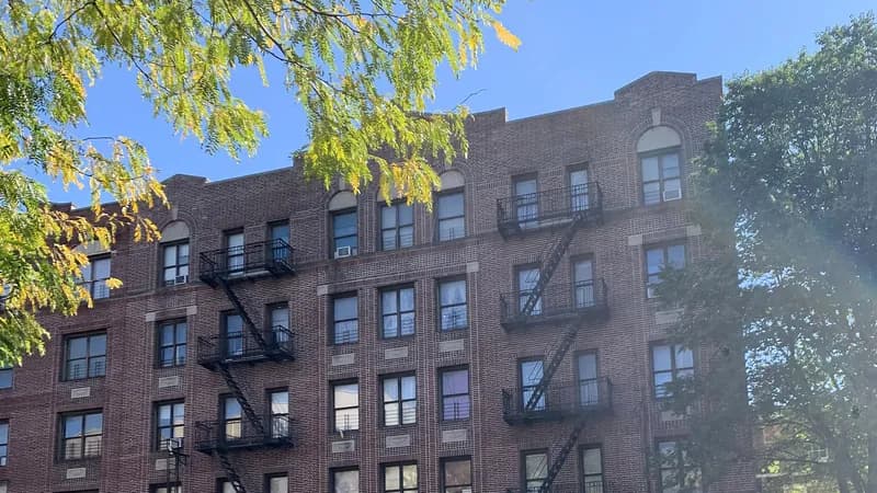 A five-story brick apartment building with fire escapes on University Avenue in the Bronx, under a clear sky.
