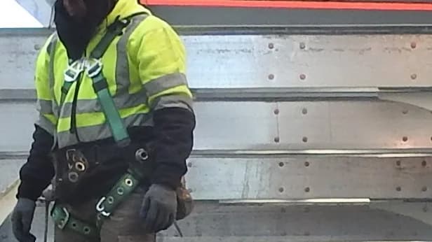 Close-up of a construction worker wearing a fall-protection harness beneath a Manhattan sidewalk shed.