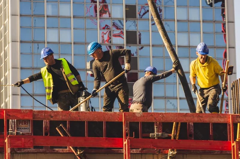 Construction workers in hard hats working beside scaffolding at a building site.
