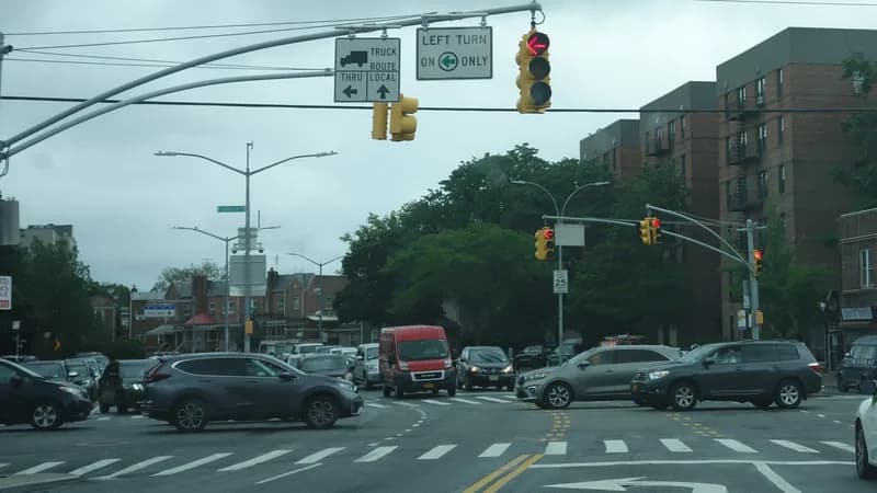 Cars turning at the intersection of Flatbush Avenue and Kings Highway in Brooklyn under a left-turn signal.