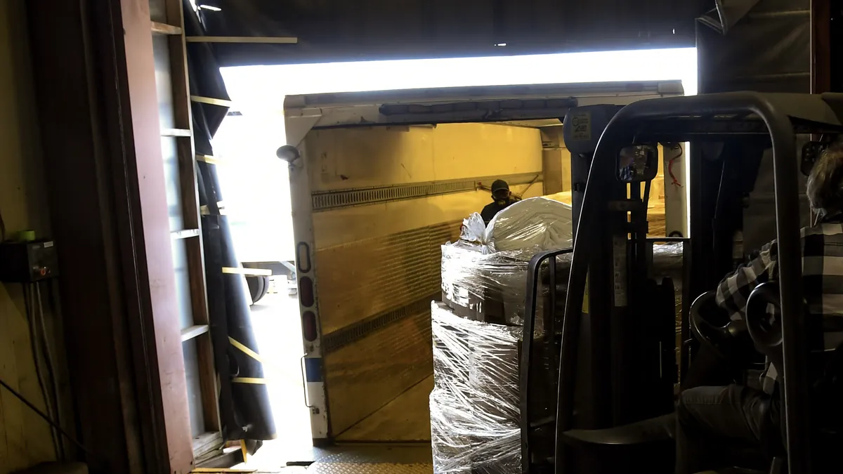 A forklift carrying a shrink-wrapped pallet across a dock plate into a trailer at a Brooklyn rail-yard storeroom.