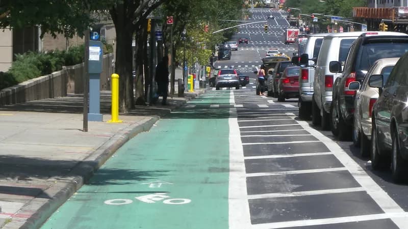 A green protected bike lane on First Avenue in Manhattan, separated from a row of parked cars by a painted buffer.