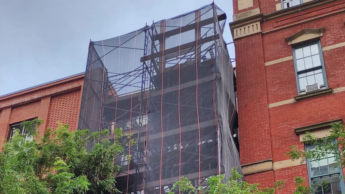 The netted frame of a building under construction between older brick buildings in Greenwich Village, Manhattan.