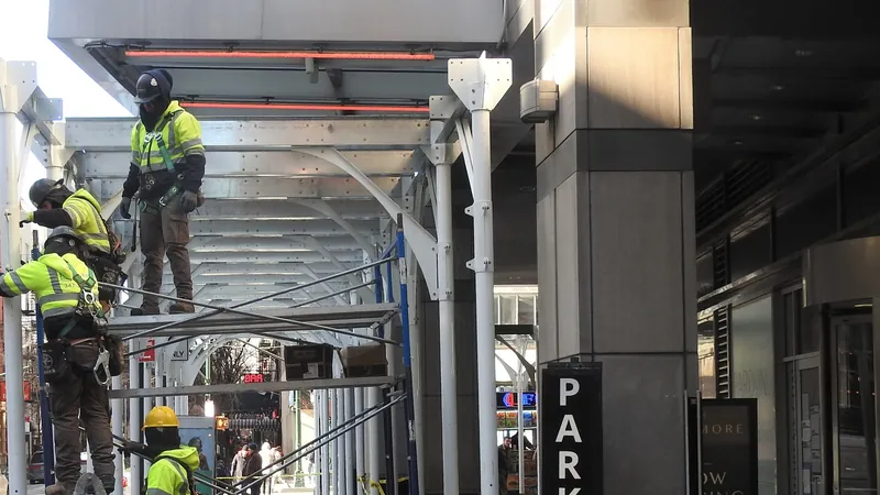 Construction workers in safety vests setting up a sidewalk shed on 47th Street in Manhattan.