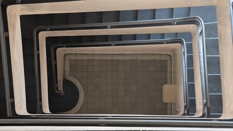 Looking down the center of an apartment building stairwell with stacked flights of stairs and metal handrails.