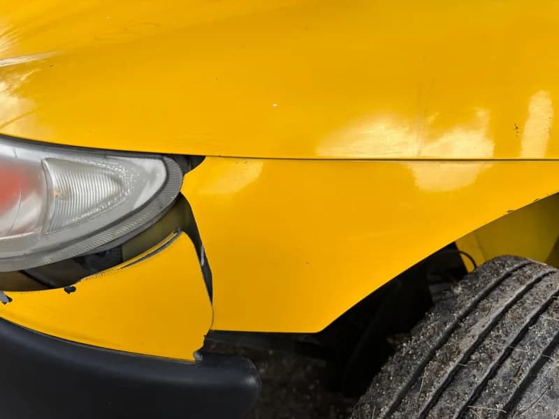 Close view of a damaged yellow car bumper and front wheel.