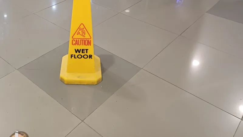 A yellow "Caution: Wet Floor" cone standing on a polished tile floor inside a shopping center.