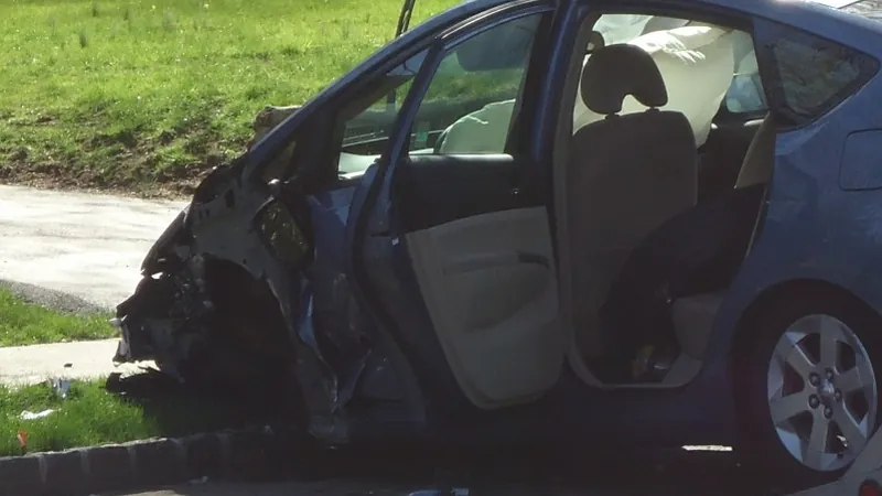 A blue hatchback with a crushed front end, its driver door open and deployed airbags hanging inside.