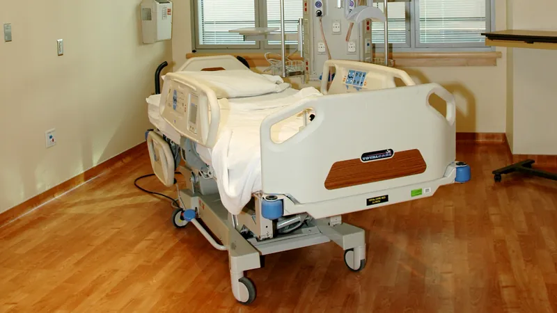 An empty patient room with an adjustable hospital bed, side rails raised.