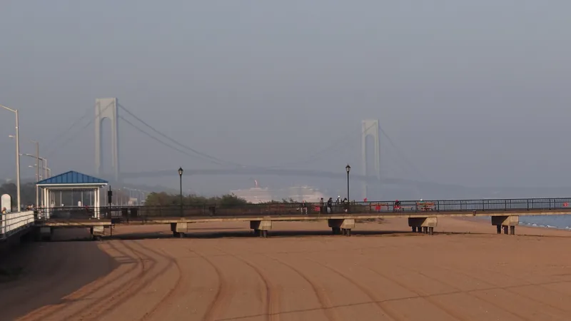 The FDR Boardwalk and beach at South Beach, Staten Island, with a gazebo and the Verrazzano-Narrows Bridge in the haze behind.