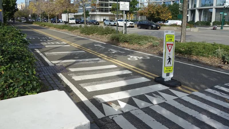 The Hudson River Greenway bike path in Manhattan where a marked crosswalk crosses it, with a yield-to-pedestrians sign beside the lane.