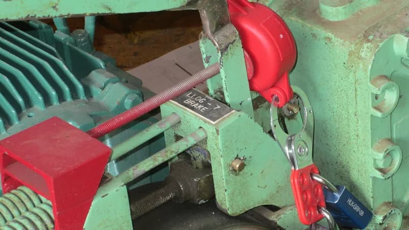 Red lockout devices and padlocks fitted to the brake of a green hoist motor.