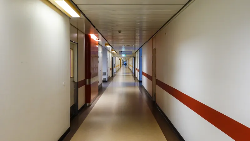 A long, empty hospital corridor with doors along both sides and a red stripe running along the wall.