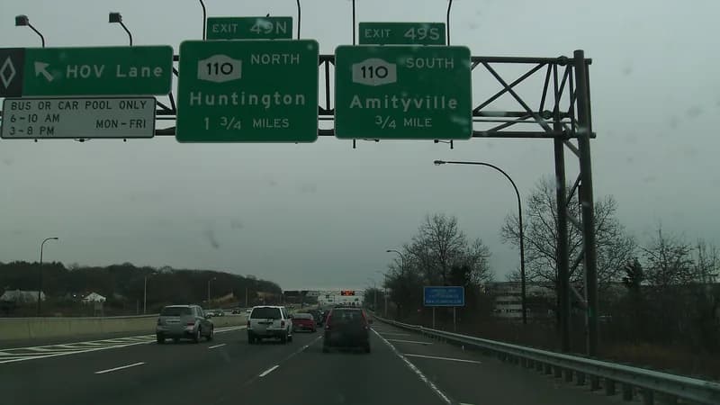 Traffic on the Long Island Expressway under overhead signs for Exit 49, Route 110 north to Huntington and south to Amityville.