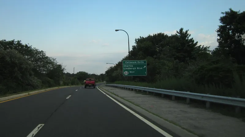 The Meadowbrook State Parkway in Nassau County with a green exit sign for the Coliseum exits and a guardrail along the shoulder.
