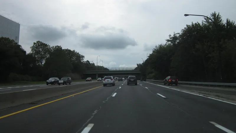 Traffic moving on the Meadowbrook State Parkway in Nassau County, with an overpass ahead and trees along the road.