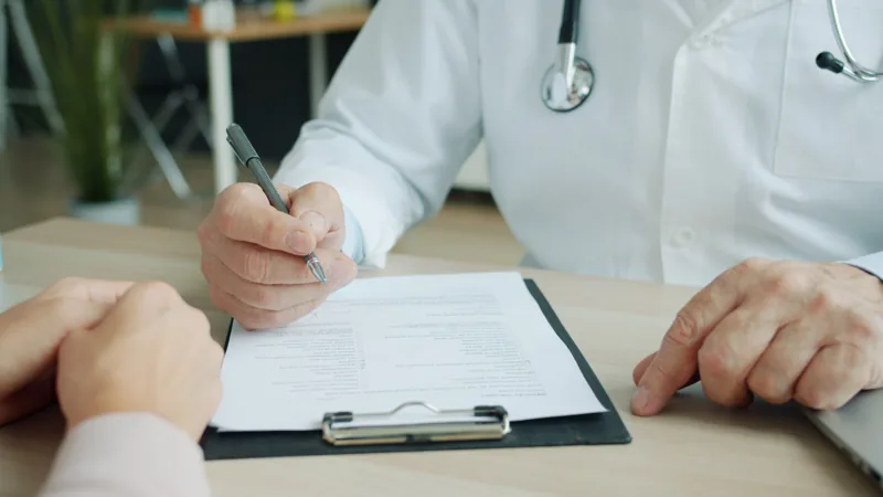 Hands of a clinician and patient beside a clipboard during a consultation.