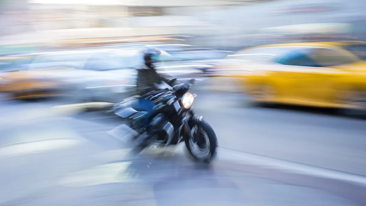 A motorcyclist riding through Midtown Manhattan traffic, with taxis blurred by motion.