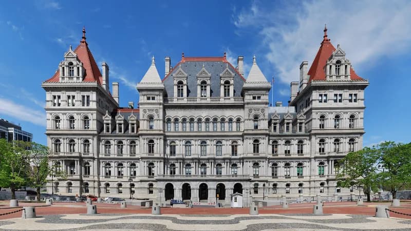 The New York State Capitol in Albany, a granite building with red-roofed towers, seen across its plaza.