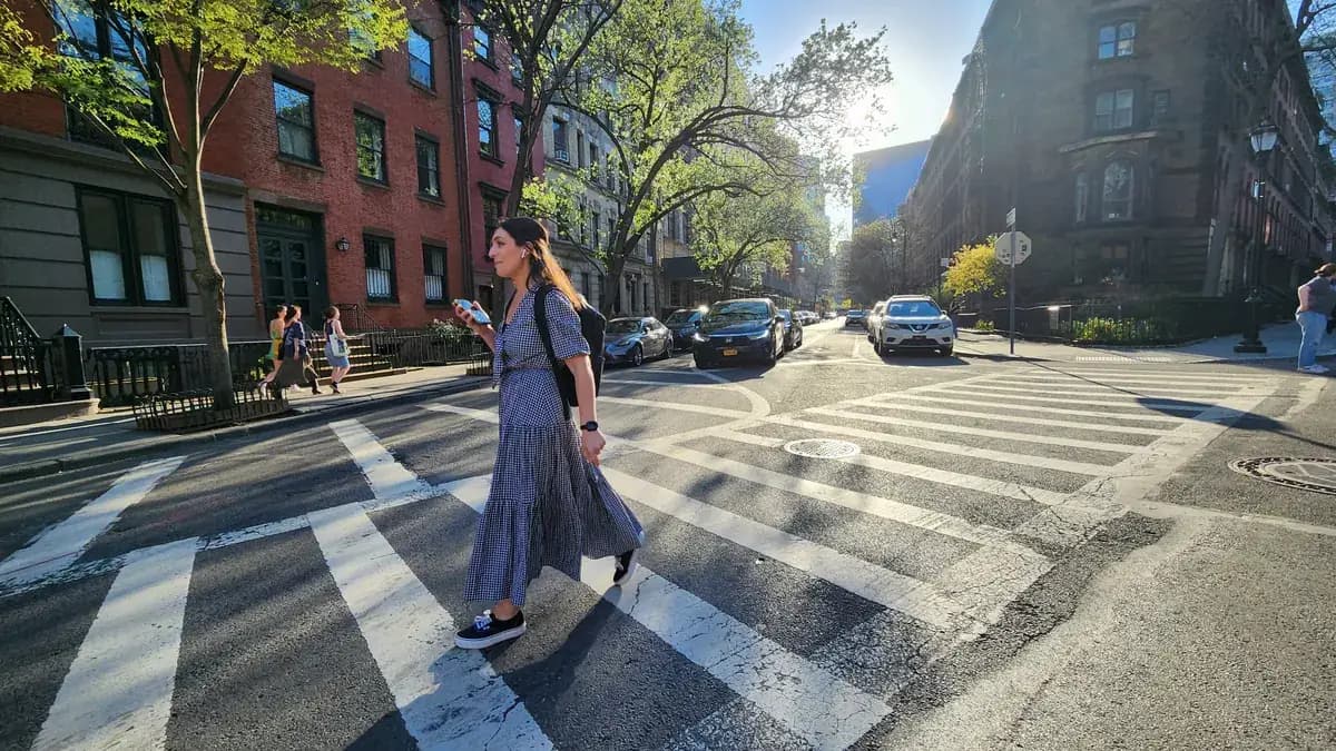 A pedestrian crossing a striped crosswalk on Stuyvesant Street in Manhattan on a sunny afternoon.