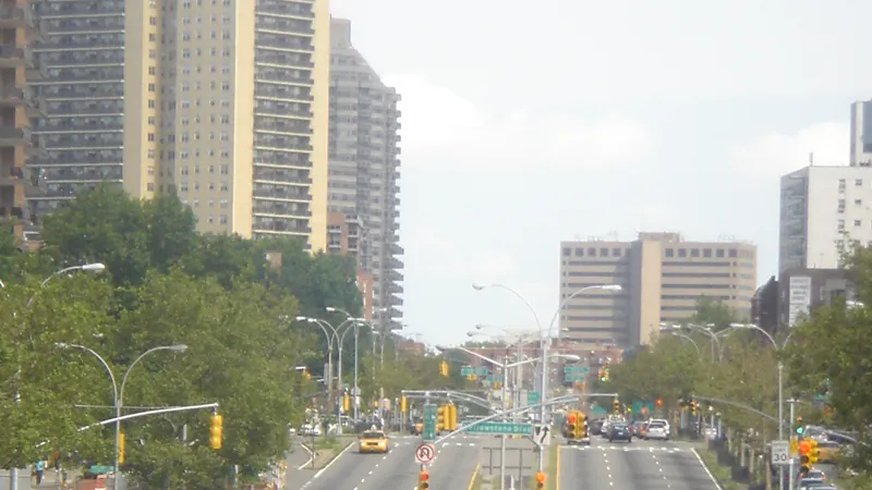Queens Boulevard approaching Yellowstone Boulevard in Forest Hills, Queens, with traffic signals, distant traffic and apartment towers.