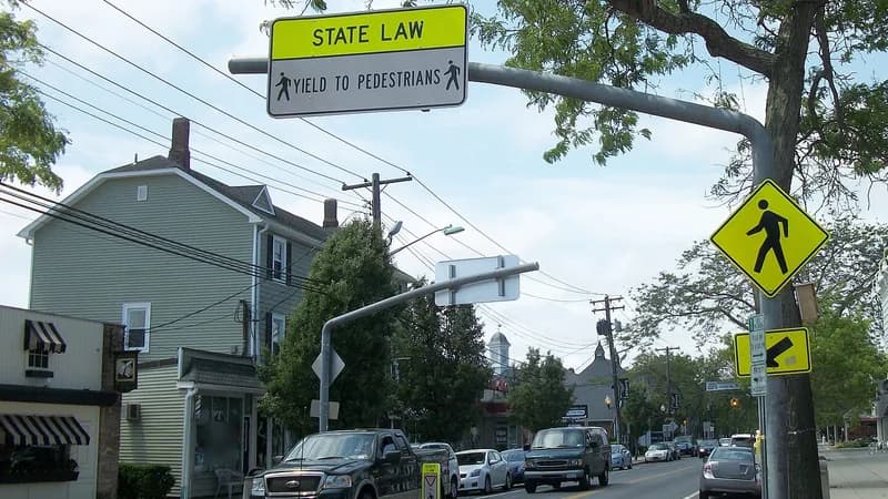A "State law: yield to pedestrians" sign above a marked crosswalk on Montauk Highway in Sayville, with a pedestrian crossing sign beside it.
