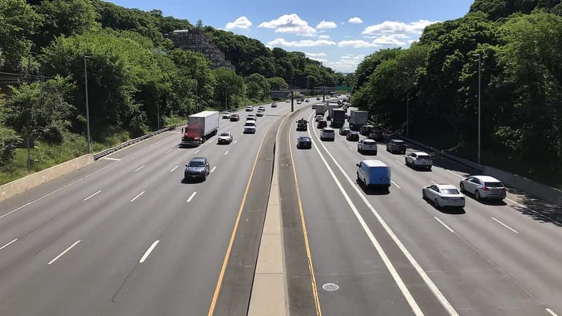 Box trucks and cars on the Staten Island Expressway between wooded slopes, seen from an overpass.