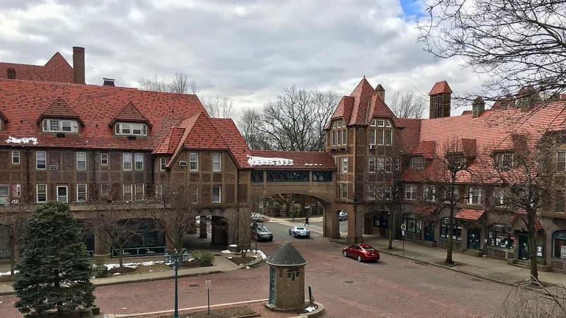 Brick buildings with red-tile roofs and an arched walkway over a small square in Forest Hills, Queens, with parked cars.