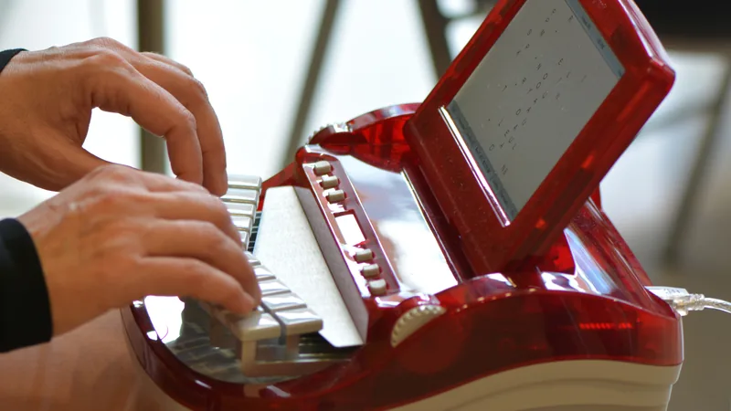 Hands typing on a red stenotype machine with a small screen showing shorthand.