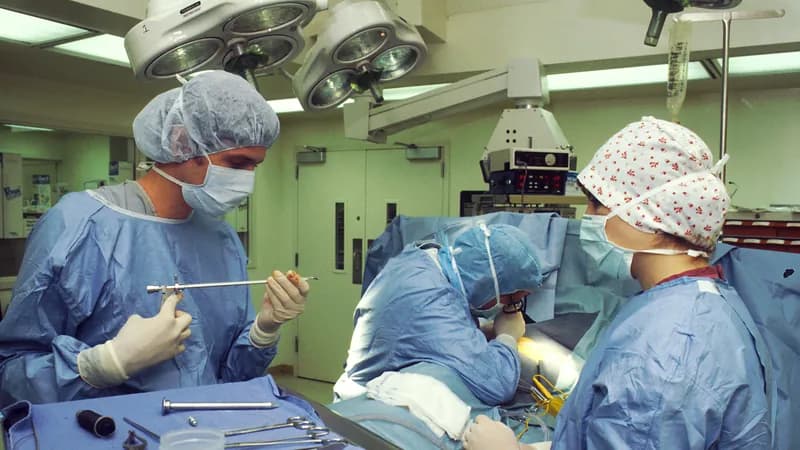 Two surgeons and a nurse in gowns and masks performing a procedure in a hospital operating room.