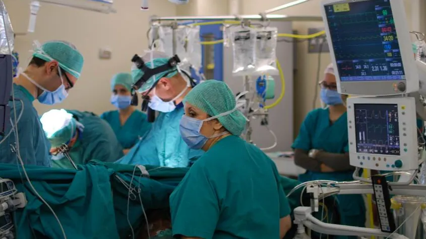 A surgical team in scrubs and masks working beside patient monitors in an operating room.