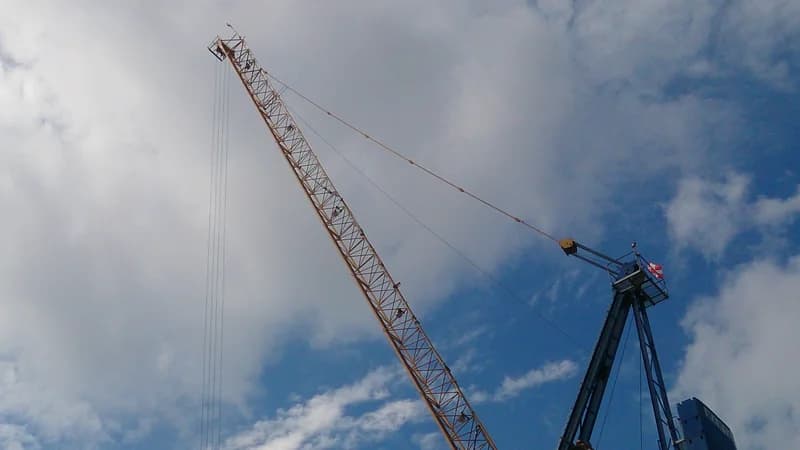 A tower crane jib and hoist cables seen from below against the sky.