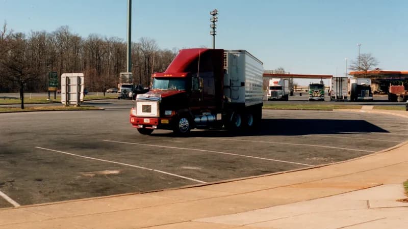 A tractor-trailer pulling through a highway truck stop parking area.