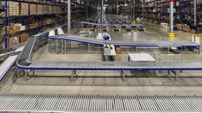 Long roller-conveyor lines running between tall pallet racks in a warehouse.